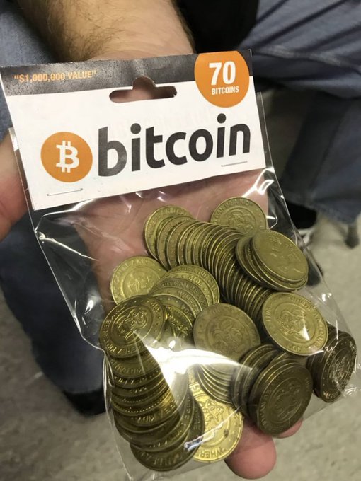 A person displays a 70-coin bag of novelty gold "Bitcoin" tokens from Temu, humorously playing along with the post's ironic claim of scoring "$1,000,000 VALUE" in BTC for a fraction of the real price on Coinbase. The orange label reads "bitcoin" with "70 BITCOINS" and "₿," poking fun at the absurdity of treating toy coins as a get-rich-quick crypto investment.