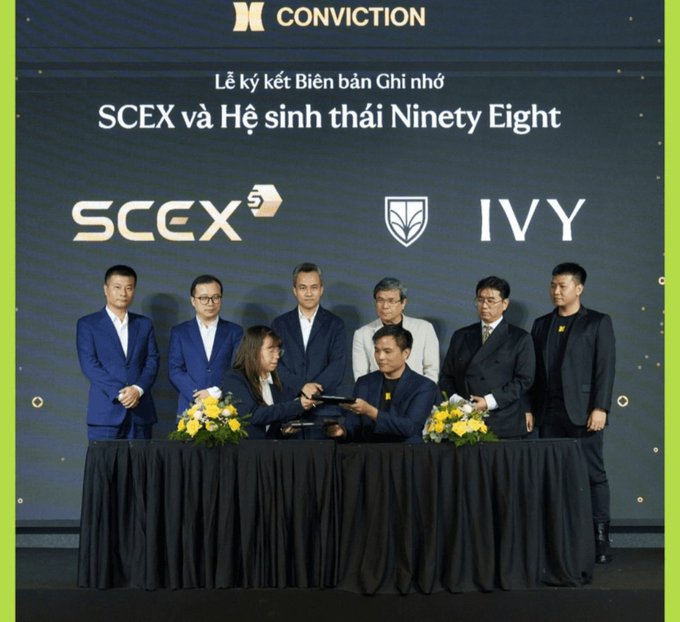 A group of people in formal wear stand behind a table during a signing ceremony, with the backdrop displaying 'CONVICTION', 'SCEX', 'IVY', and Vietnamese text referencing a memorandum signing.