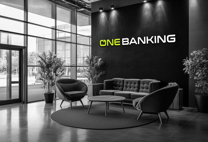 The image shows a modern office space with large windows that let in plenty of natural light. The room features two couches placed against each other facing a black wall adorned with a logo for "One Banking" company, which is known for its innovative approach to financial services and digital transformation. A coffee table sits between the couches, and there are potted plants on either side of the room, adding a touch of greenery to the space. The office appears to be designed for collaboration and creativity, with an emphasis on sustainability and eco-friendliness.