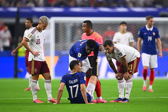 A French player wearing the "SALIBA 17" jersey sits on the pitch surrounded by teammates and Belgian opponents (including one wearing number 21), while the accompanying post references France's ("Mbappe's") defeat and upcoming matches at the World Cup.