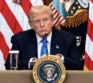 President Donald Trump sits behind a podium bearing the Presidential Seal, with American flags and a glass of water visible in the background, as the post highlights his previous calls to eliminate taxes on Bitcoin and crypto transactions.