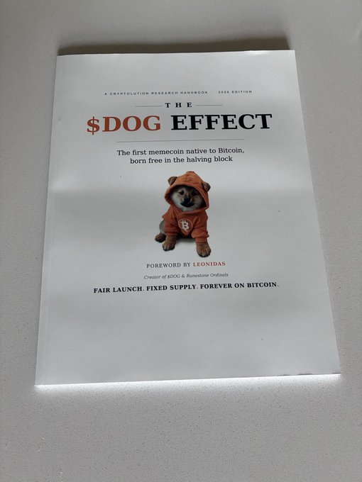 A book titled 'THE $DOG EFFECT' with subtitle 'The first memecoin native to Bitcoin, born free in the halving block' featuring a Shiba Inu puppy in an orange hoodie, foreword by Leonidas.