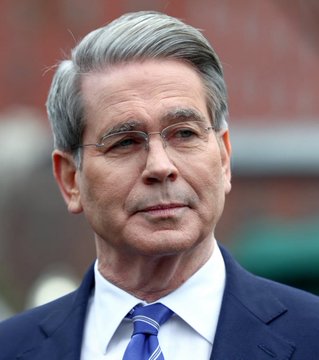 A close-up portrait of Treasury Secretary Scott Bessent, shown in a dark suit, white shirt, and striped blue tie, looking off-camera. The image accompanies a statement about his comments attributing the USD's declining share of global reserves to actions by China and Russia.