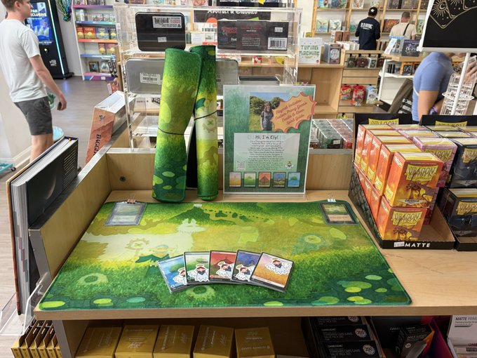 A Pokémon Trading Card Game display in a retail store featuring a 'He Lx Epi!' starter deck set with green-themed playmats, oversized card props, and booster boxes stacked nearby.