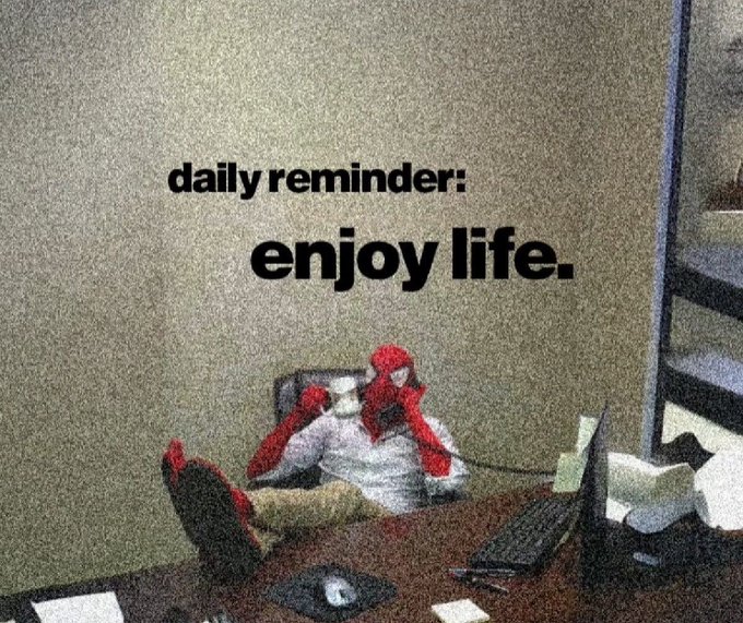 A grainy photo of a person relaxing at a desk with feet up and on a phone call, overlaid with the text 'daily reminder: enjoy life.'