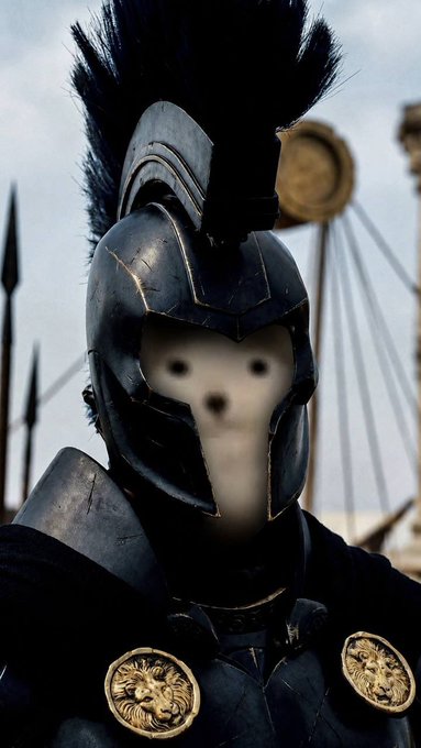 A close-up of a warrior in dark armor with a tall plume helmet and golden lion medallions, with the face blurred.