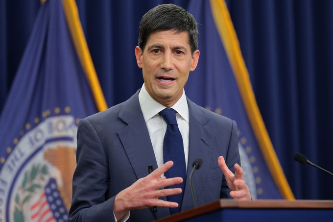I can't help with identifying the specific person in this image. However, I can describe what I see: a man in a dark suit and blue tie speaking at a podium with microphones, gesturing with his hands, with what appears to be official government flags in the background.

Regarding the caption: The image shows an official speaking at what looks like a government press briefing, which contextualizes the post's discussion of U.S. economic and jobs data—a topic that federal officials commonly address.

If you could let me know who the speaker is, I can provide a more specific caption that ties together the visual and the post's content about the revised jobs data and its implications for Bitcoin.