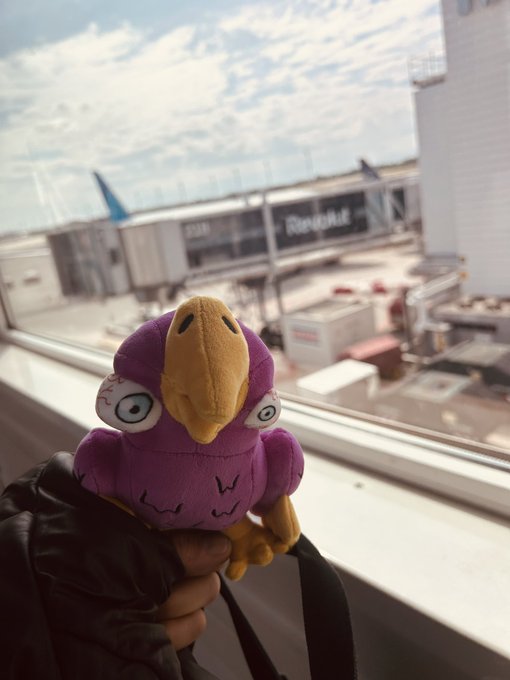 The image features a person holding a purple plush toy bird, which appears to be a parrot-like stuffed animal with a black head and yellow body. The person is wearing a black jacket over their shoulder. In the background, there are several airplanes visible outside an airport window, suggesting that this scene takes place at an airport. The post includes text about a claimed Allo Pass Utility item, which could be related to the toy or possibly some other product associated with the Allo Pass utility service.

The image seems to be promoting a product or service related to the Allo Pass utility, as it is described in the caption. This might indicate that the person holding the plush toy bird is either a customer of the Allo Pass utility or has purchased the item for someone else who uses the Allo Pass utility.