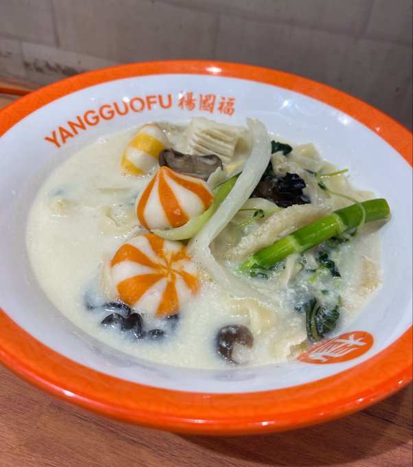 A bowl of soup with decorative orange and white fish balls, mushrooms, bamboo shoots, and vegetables in a creamy broth, served in a bowl labeled 'YANGGUOFU' with Chinese characters.
