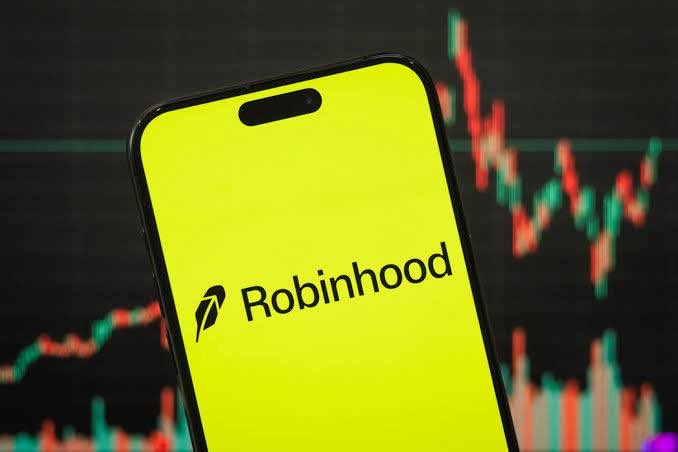A smartphone displaying the yellow Robinhood logo app against a background of a stock market chart with red and green candlesticks.