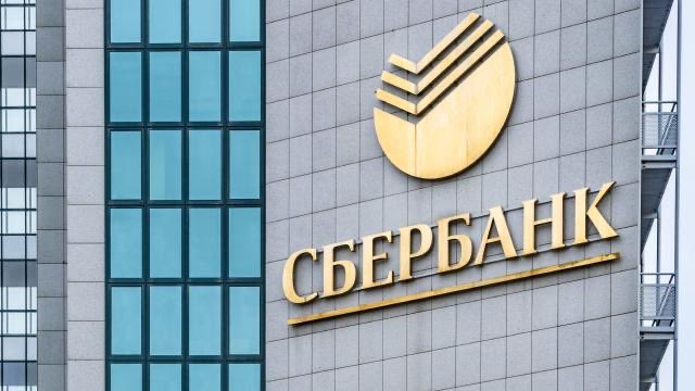 The exterior of a modern building featuring a large golden logo and the text "СБЕРБАНК" (Sberbank) mounted on a tiled facade.
