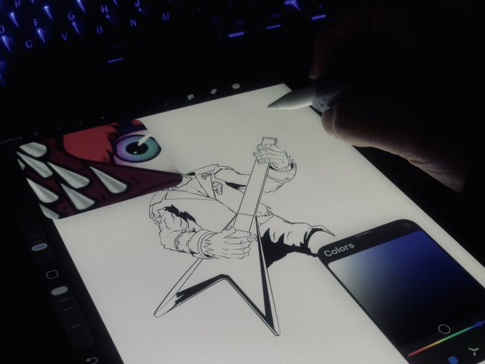 A dark workspace showing a digital drawing tablet displaying an anime character sketch and a menacing red creature illustration, with a stylus being used over a backlit keyboard.
