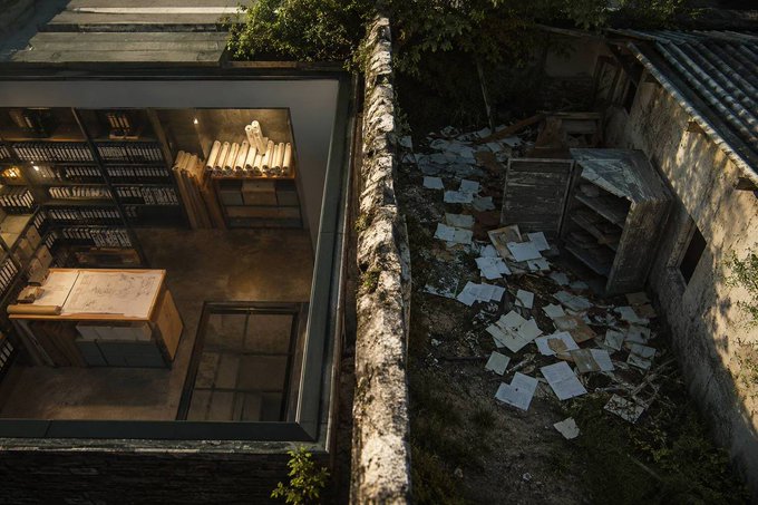 An overhead view showing a contrast between a neat indoor library/archive room on the left and an outdoor courtyard scattered with discarded papers on the right.