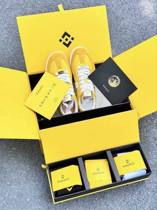 A yellow Binance-branded gift box containing yellow sneakers, socks, and other merchandise with the Binance logo.