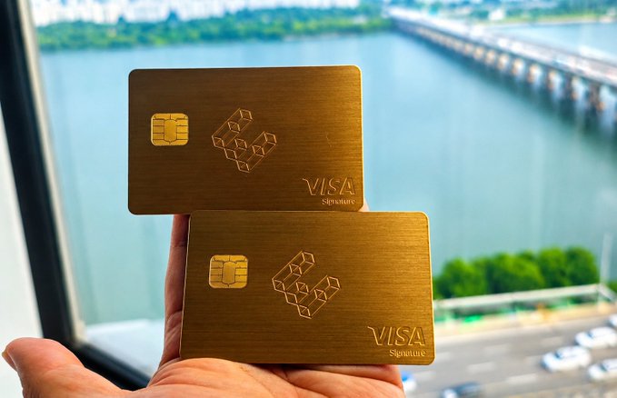 A hand holds two gold Visa Signature metal cards featuring the ether.fi logo, displayed against a backdrop of a waterfront bridge and cityscape, promoting the EtherFi VIP card experience shared in the post.