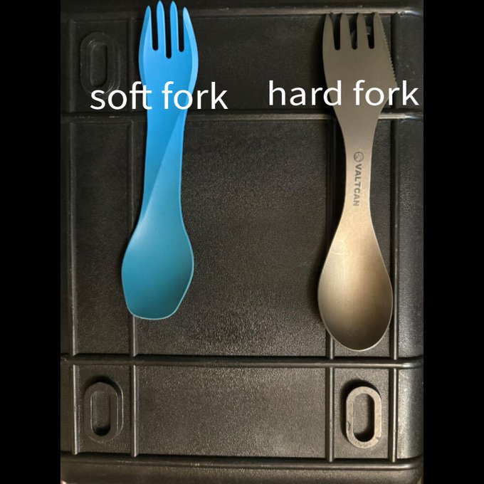 The image shows a blue plastic "spork" (labeled "soft fork") next to a metal gray spork (labeled "hard fork"), cleverly visualizing the cryptocurrency concept of soft forks versus hard forks as a humorous "pick one now" choice. The metal spork is branded "VALTCAN."