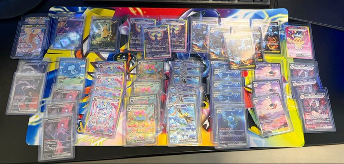 An extensive Pokémon trading card collection laid out on a colorful playmat, featuring numerous holographic and rare cards arranged in rows.