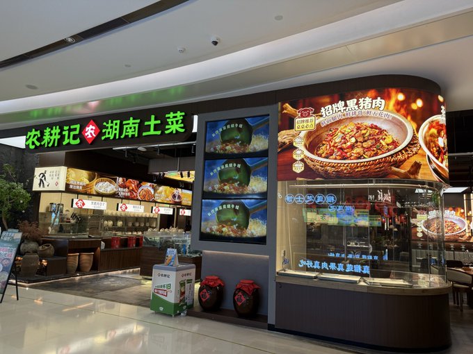 The entrance to a Chinese restaurant with signs reading '农耕记 湖南土菜' and displays featuring various dishes.