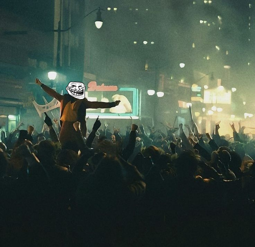 The image shows a large crowd of people gathered together, with some individuals holding up signs or banners. One person among them has a face painted on their head that reads "Ugly", adding an element of humor to the scene. The background features buildings and street lights, suggesting an urban setting for this event. The post includes text such as "Nothing can stop what's coming... $TROLL the markets". This phrase is likely meant to be a humorous commentary on the current situation or trend in the image.