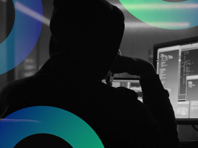 A silhouetted figure in a hoodie sits before glowing computer monitors displaying code, evoking the classic imagery of a cybercriminal at work. This visual pairs with the post about NEAR Protocol's Intents feature, which helped protect Bitget from a $50 million hack only for the platform itself to suffer a $3.8 million exploit due to a vulnerability between Omni's deposit and withdrawal systems and its smart contract.