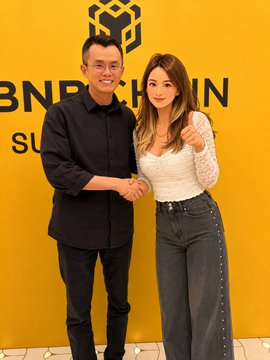 The caption is: A young man in a black shirt and a young woman in a white lace top pose together in front of a yellow backdrop displaying the "BNB CHAIN SUMMIT" logo, with the man shaking the woman's hand in a congratulatory gesture. The image accompanies a post reflecting on completing CZ's book "Binance Life" and one's multi-year journey at Binance and in crypto, capturing a celebratory industry event moment.