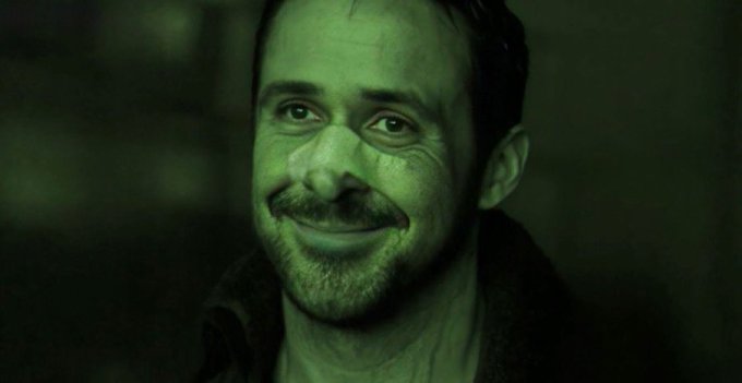 A close-up portrait of a smiling man with a beard and mustache, bathed in green light.