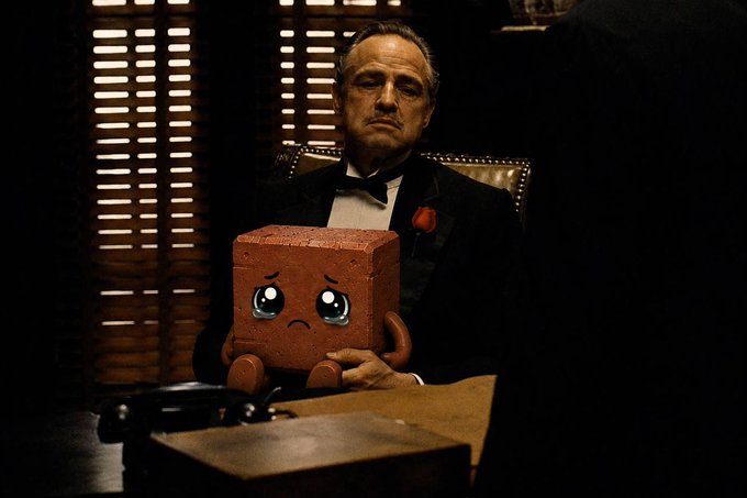 An AI-edited parody image of Don Vito Corleone (The Godfather) sitting in a leather chair holding a sad-faced red Lego brick instead of a cat.