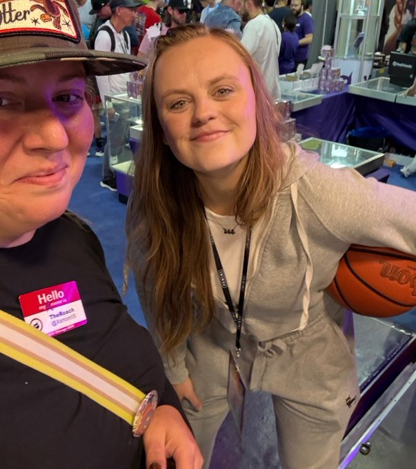 Two women pose at what appears to be a convention, with one wearing a 'Hello, my name is TheBeach' badge.
