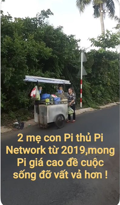 A street food vendor stands behind a metal cart on a paved road, with Vietnamese text overlay reading: '2 mẹ con Pi thủ Pi Network từ 2019, mong Pi giá cao để cuộc sống đỡ vất vả hơn !' (A mother and child holding Pi Network since 2019, hoping Pi's price rises for a less difficult life!).