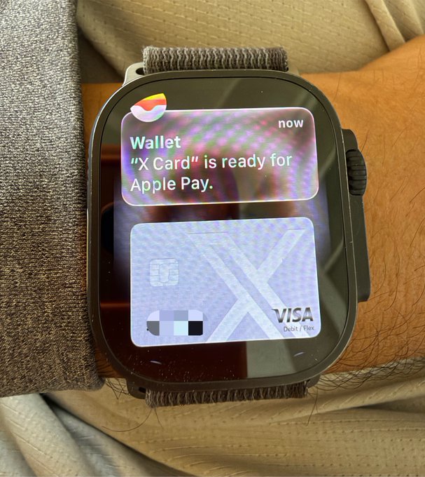 An Apple Watch displays a notification that "X Card is ready for Apple Pay" alongside a Visa debit card with a large "X" design. The image visually represents the creator's excitement about integrating the X (formerly Twitter) branded debit card into their daily life, with the accompanying text highlighting both the convenience of wearable payments and a wish to invest in xAI stock.