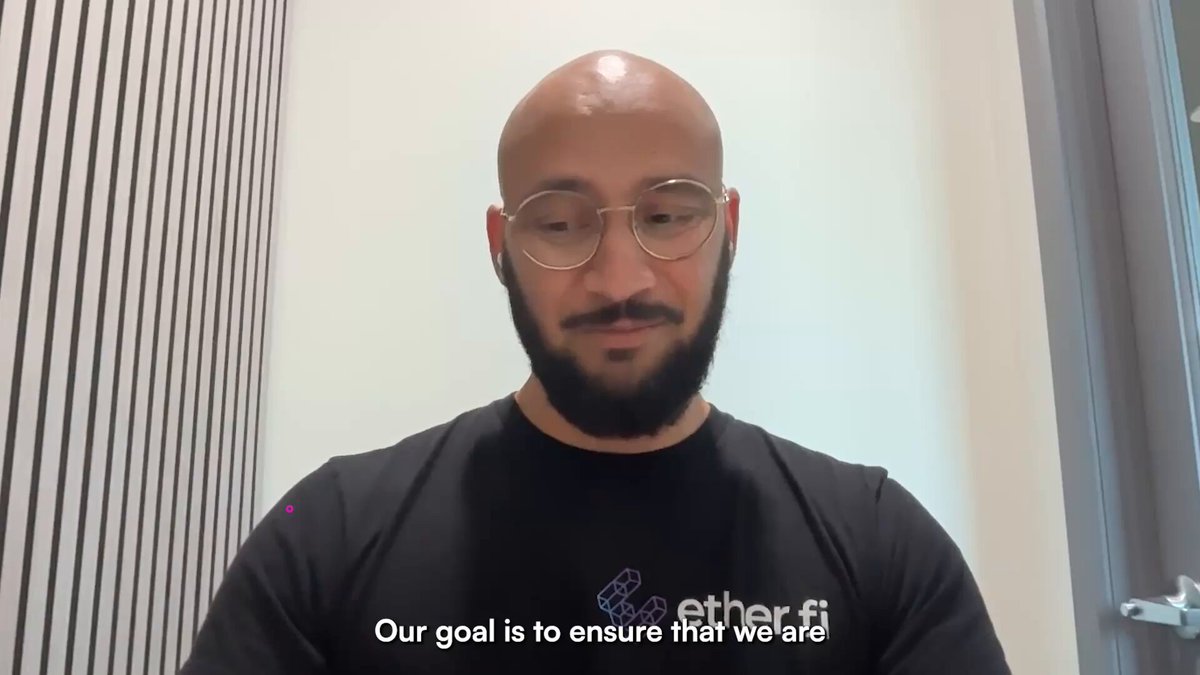 The image shows a man wearing glasses, sitting down with his head resting on his hand while looking at the camera. The background of the image features a white wall with black stripes running across it. There are also some text elements visible in the image that read "Our goal is to ensure that we have a secure and transparent ecosystem".