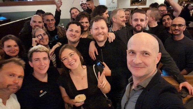 Group selfie taken at what appears to be a social gathering, featuring a woman holding a Hublot-branded microphone and the selfie-taker wearing a suit jacket.