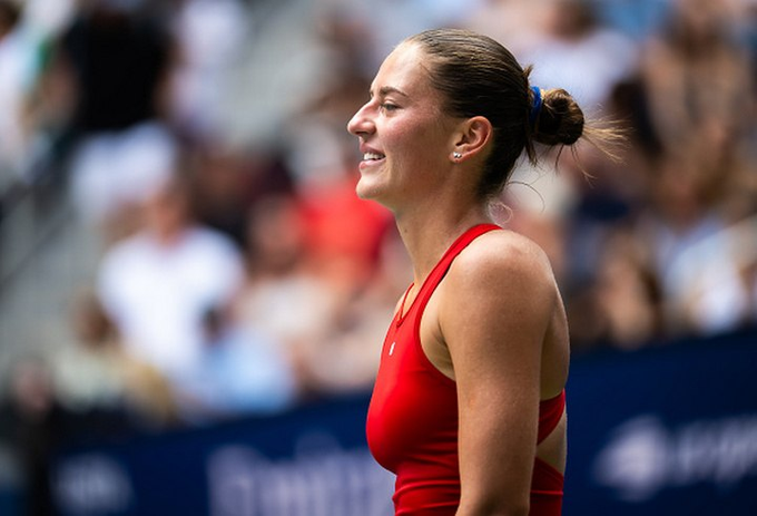 A female tennis player in a red outfit smiles while on the court during a match.
