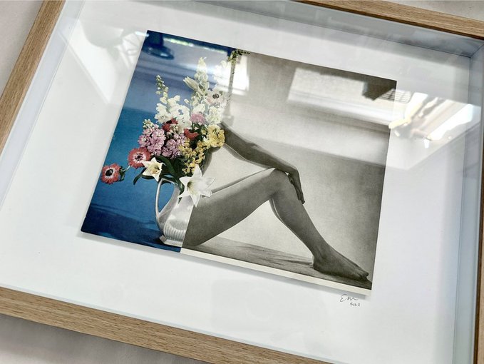 A framed photographic print displayed at an angle, featuring a surreal black-and-white image of a woman's legs blending into a blue background with a vibrant bouquet of flowers, signed "Esko 2021" in the lower right corner. The physical artwork shown relates to the post as a tangible, gallery-ready piece being sold alongside its digital counterpart on SuperRare.