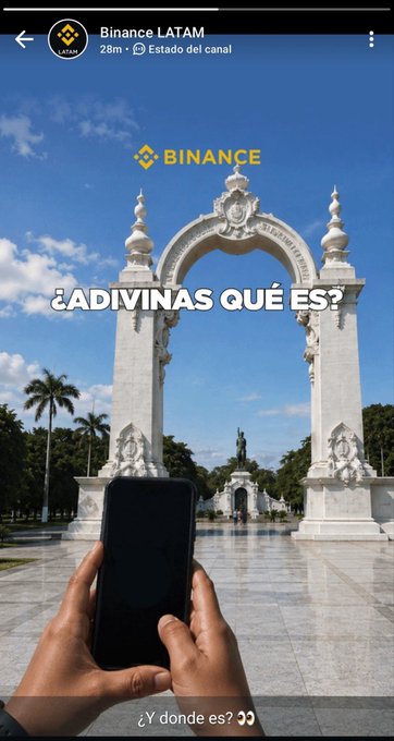 A screenshot of a Binance LATAM Telegram post showing a white monument arch with a person holding a phone in the foreground, overlaid with "BINANCE" and "¿ADIVINAS QUÉ ES?" / "¿Y dónde es?" text. The post references the Arc of the Battle of Carabobo, a Venezuelan landmark, hinting that Binance's card launch date coincides with the battle's anniversary.