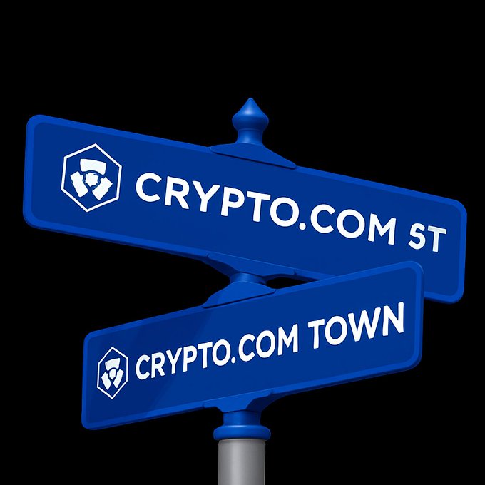A cartoon-style blue street signpost displaying two intersecting signs: the top reads "CRYPTO.COM ST" and the bottom reads "CRYPTO.COM TOWN," each featuring the Crypto.com hexagon logo. This humorous visual reinforces the post's joke about Crypto.com being at every corner, suggesting the brand (along with Cronos/$CRO) has its own dedicated neighborhood.