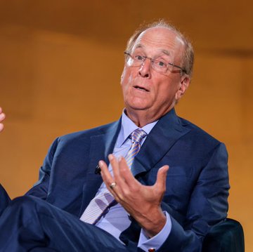 A distinguished older gentleman in a blue suit and patterned tie gestures expressively while speaking, appearing to be engaged in a formal interview or discussion. The image is associated with a news post about BlackRock ETF clients purchasing $15.35 million worth of Ethereum ($ETH), suggesting he may be discussing cryptocurrency or ETF-related matters as a financial expert or executive.