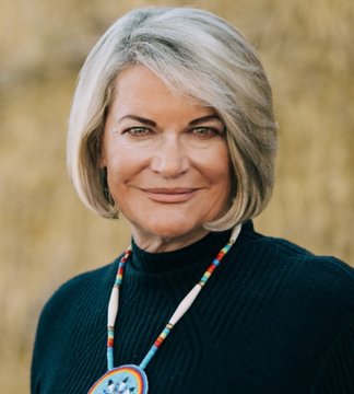 The image features a woman wearing a black sweater and necklace with colorful beads. She has short blonde hair, giving her a youthful appearance. The background of the photo appears to be a wall or a building, which could potentially be an office space for the Senator Lummis. The text "SENATOR LUMMIS: ?" suggests that she is addressing the public and possibly discussing matters related to the clarity act in America.

The image seems to be a portrait of the woman with her hair styled in a way that complements her overall appearance, making it an appealing visual representation of the Senator Lummis's stance on the clarity act.