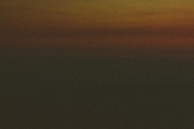 A dark, low-light photograph showing only a faint, blurry band of orange and brown light near the top of the frame.
