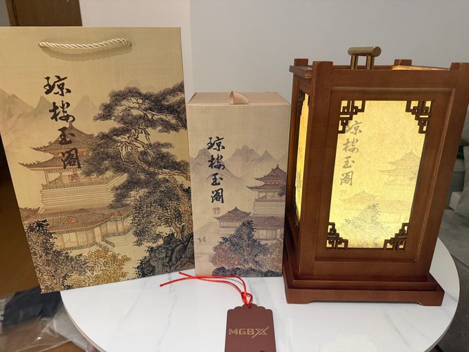 The image features a wooden table with three items displayed on it, including a small lantern, a brown paper bag, and a tag. The lantern has an Asian design that includes trees and mountains, while the brown paper bag also has an Asian design. A red tag is attached to one of these items. The objects are arranged in such a way that they create a visually appealing display, showcasing the craftsmanship and cultural influences present in each item.