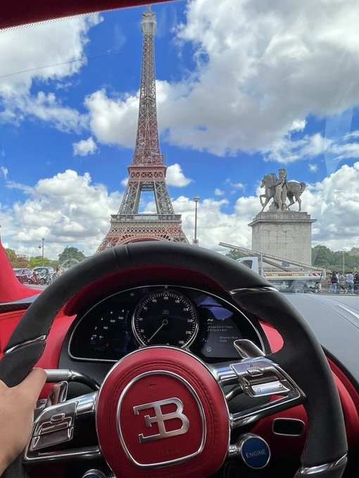 A Bugatti driver's perspective from inside the cockpit, with the steering wheel's iconic "EB" logo and "ENGINE" start button visible, overlooking the Eiffel Tower and Pont d'Iéna statue against a partly cloudy Paris sky—an opulent scene that contrasts with the post's discussion of digital sovereignty and data privacy control offered by ARC versus frontier AI models.