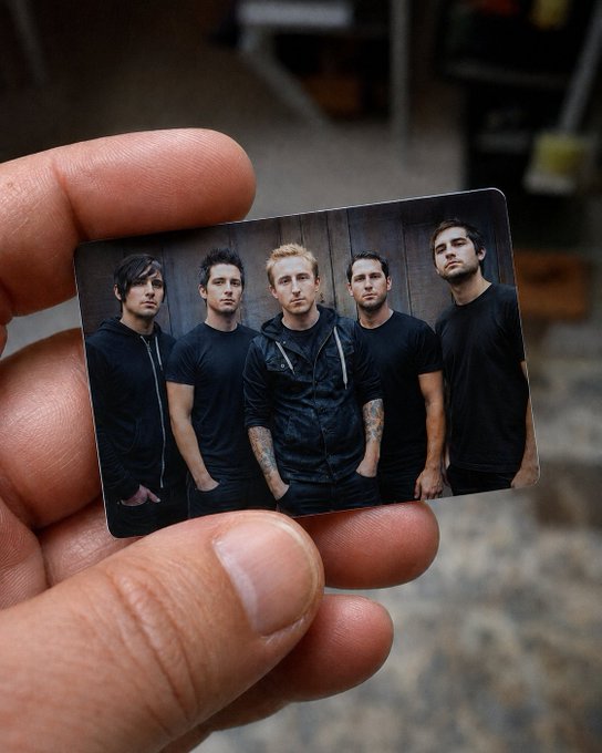 A hand holding a small collectible card featuring a photograph of five men in dark clothing, likely a band, posed against a wooden backdrop.