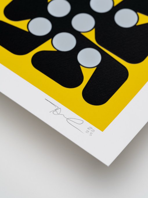 A close-up of a corner of an art print with a yellow background featuring black shapes with grey circles, signed and dated '2023'.