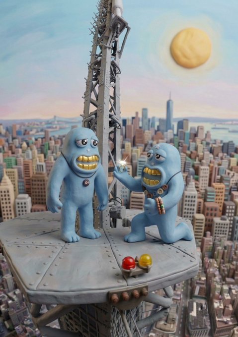 Two blue claymation characters with gold teeth standing atop a skyscraper spire overlooking a New York City skyline, one holding a glowing diamond while the other wears a pendant.