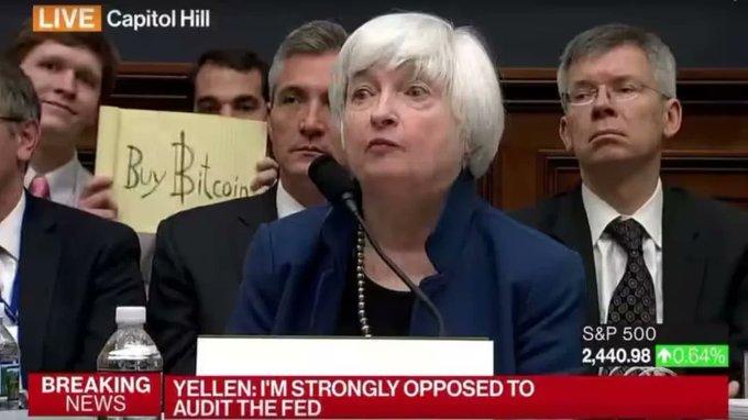Janet Yellen testifies at a Capitol Hill hearing with a "Buy Bitcoin" sign held behind her, while the chyron reads "YELLEN: I'M STRONGLY OPPOSED TO AUDIT THE FED" and the S&P 500 shows 2,440.98, capturing the moment referenced in the post about a young man silently protesting monetary policy behind the Fed Chair nine years ago.