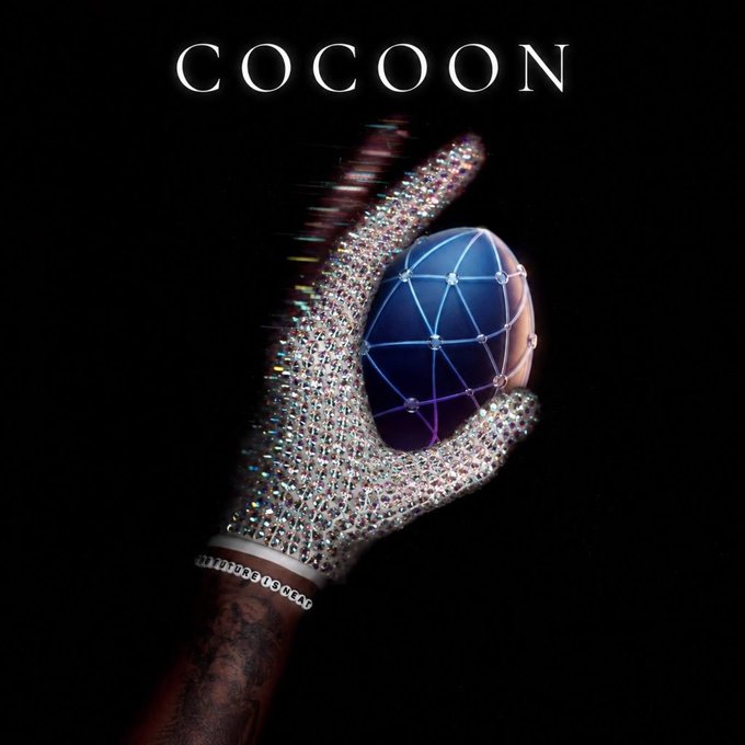 The image features the word "COCOON" at the top with a hand adorned in a sparkling jeweled glove holding an oval gemstone marked with a geometric network pattern, set against a black background—symbolizing the careful handling and protective grip needed around a token like $COCOON while awaiting its bottom, much like cradling a precious gem before its market recovery.