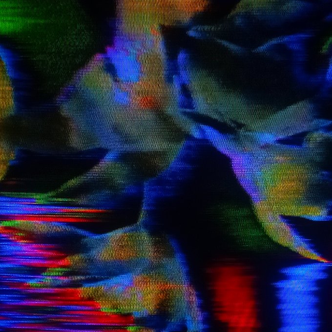 An abstract, glitchy image featuring distorted pixelated colors in dark blues, reds, greens, and purples with visible screen texture.