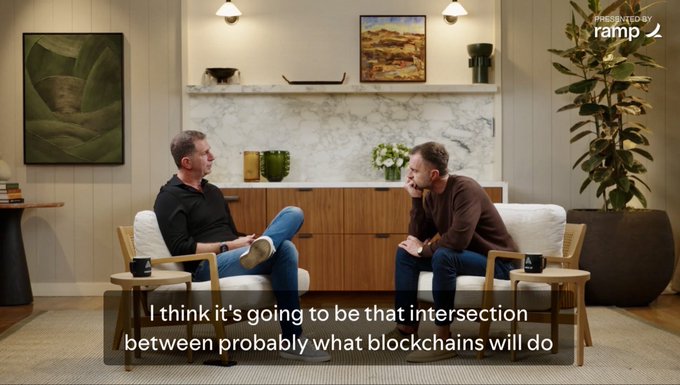 A screenshot from a presentation presented by Ramp, showing two men seated in armchairs conversing, with a subtitle reading: 'I think it's going to be that intersection between probably what blockchains will do'.