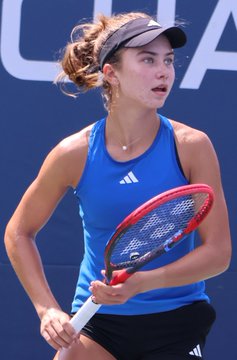 A female tennis player in a blue Adidas tank top and white visor holding a tennis racket on a court.