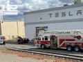 An outdoor photo of a red Tesla fire truck parked in front of a large industrial building with 'TESLA' written on it.